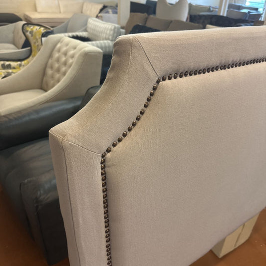Close-up of a beige upholstered chair with nailhead trim in a furniture store.