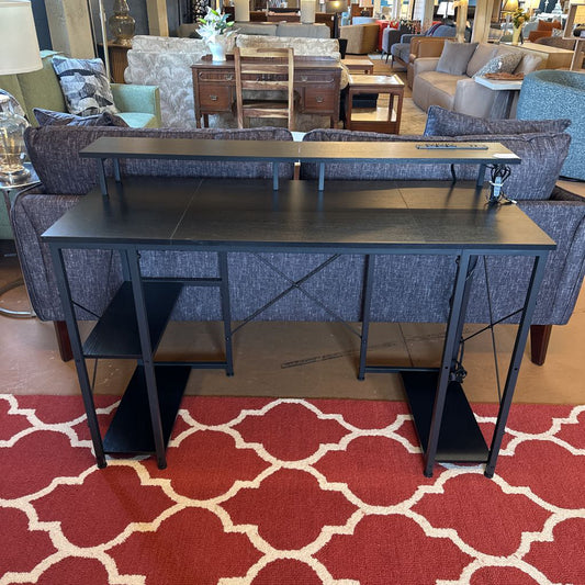 Black metal desk in a furniture store with blue upholstered chairs and a red patterned carpet.