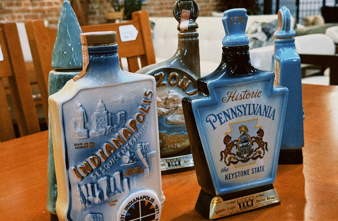 A row of unique ceramic Jim Beam bourbon decanters on a wooden table, featuring colorful illustrations and text for Indianapolis and Pennsylvania.