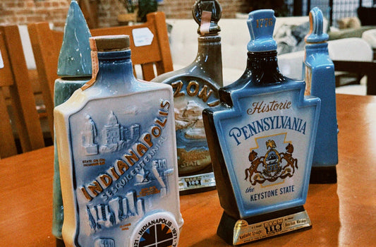 A row of unique ceramic Jim Beam bourbon decanters on a wooden table, featuring colorful illustrations and text for Indianapolis and Pennsylvania.