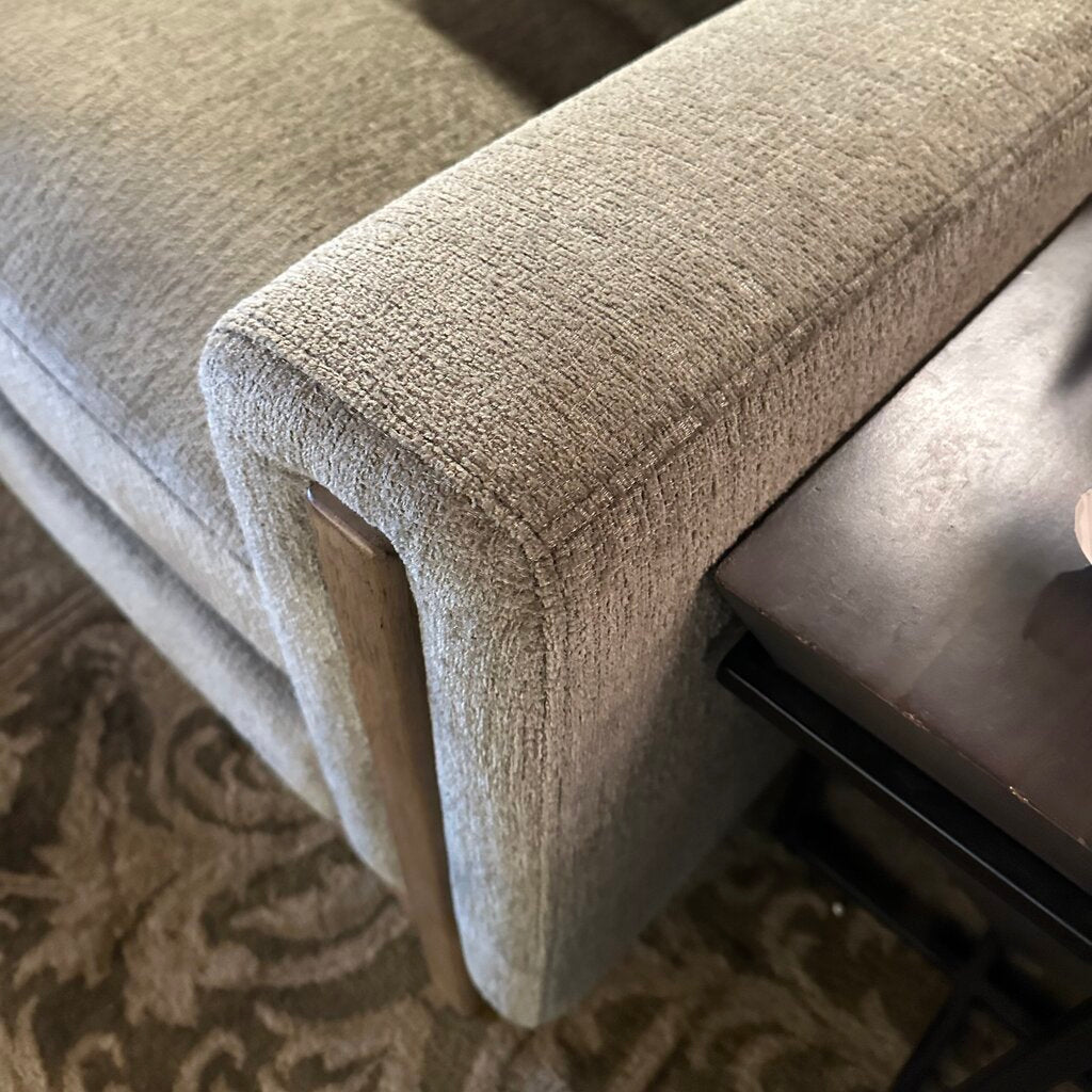 Close-up of a textured beige upholstered chair corner on a patterned rug.