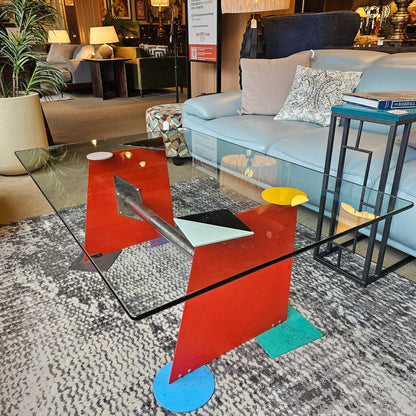 Modern glass coffee table with colorful geometric base in a living room setting
