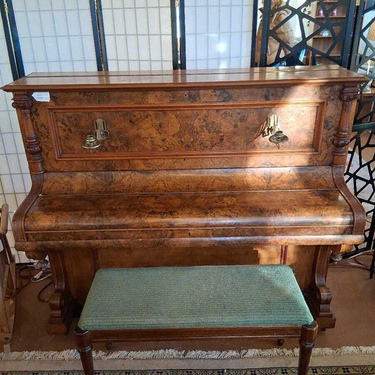 Wooden piano with a green cushioned bench in a tiled room.