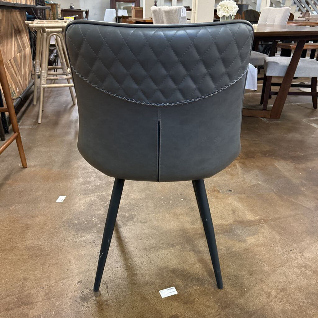 Gray quilted chair with black legs on a concrete floor in a warehouse setting.