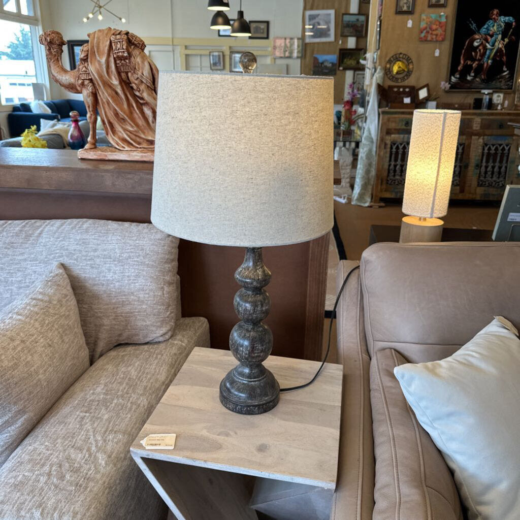 Table lamp on a side table in a living room setting with another lamp in the background.