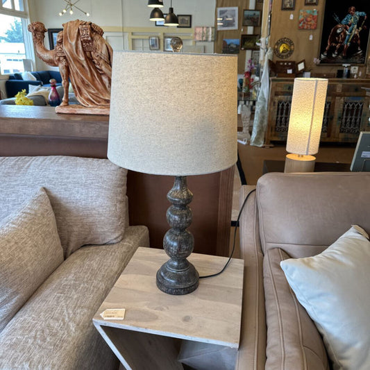 Table lamp on a side table in a living room setting with another lamp in the background.