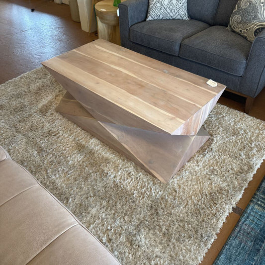 Wooden coffee table on a beige rug with a gray sofa and beige chair in the background.