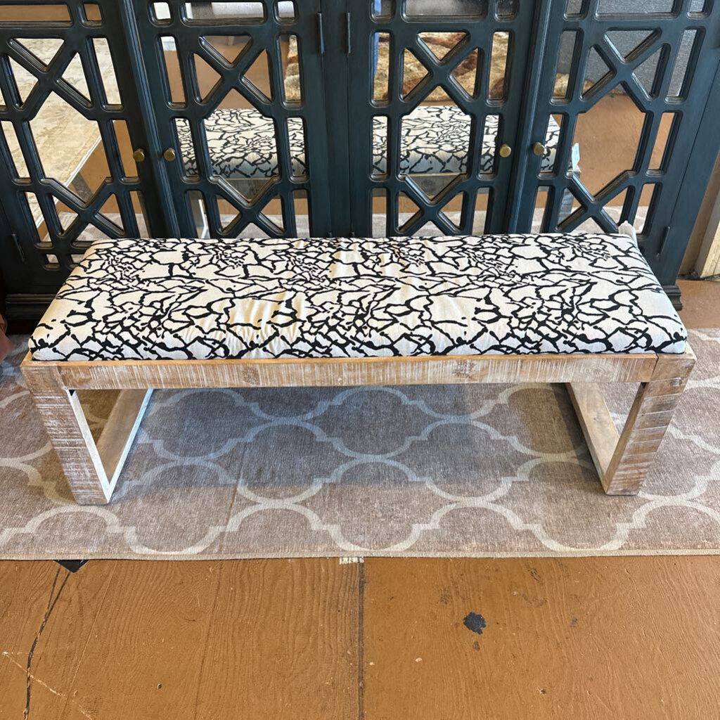 Wooden bench with a black and white patterned cushion on a wooden floor.