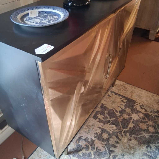 Copper cabinet with a black countertop and blue and white plate on a patterned rug.
