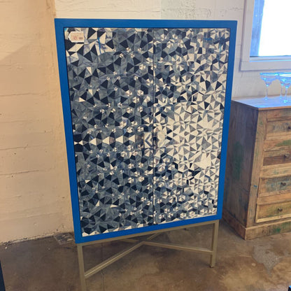 Cabinet with geometric patterned door on a stand against a wall.