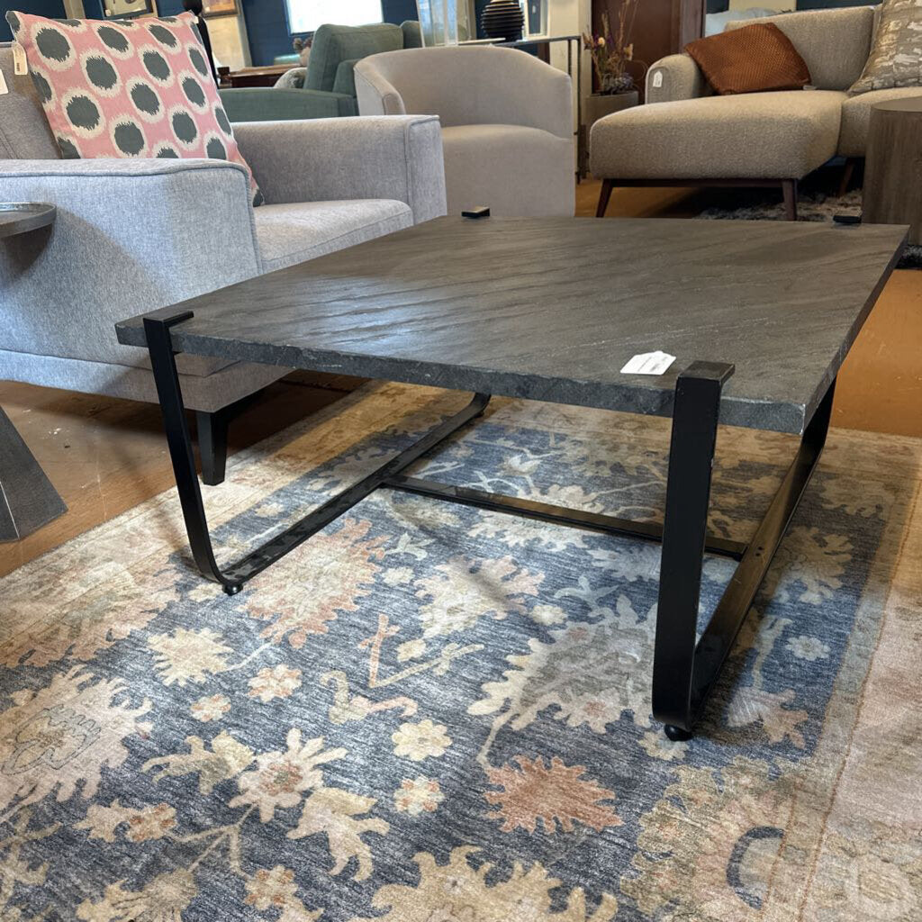 Dark wooden coffee table with metal legs on a patterned rug in a furniture store.