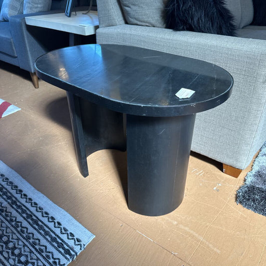 Black side table in a room with gray sofa and patterned rug