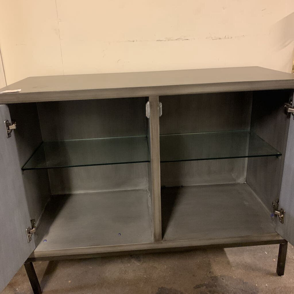 Gray metal cabinet with glass shelves against a plain wall.