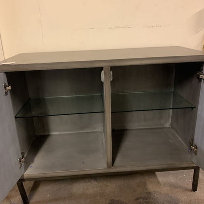 Gray metal cabinet with glass shelves against a plain wall.