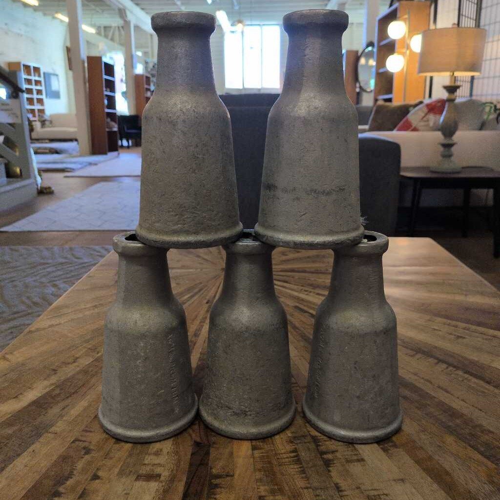 Five rustic clay bottles stacked on a wooden table in a room with furniture and decor.