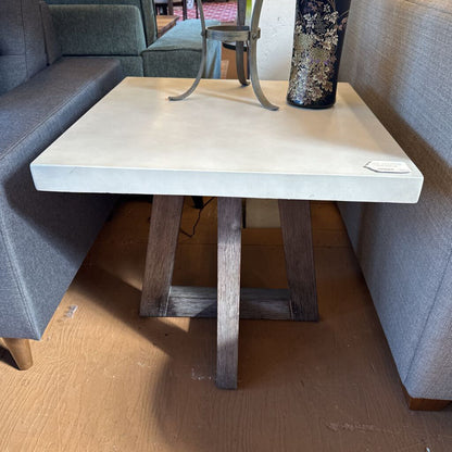 Small table with a concrete top and wooden legs in a room with gray couches.