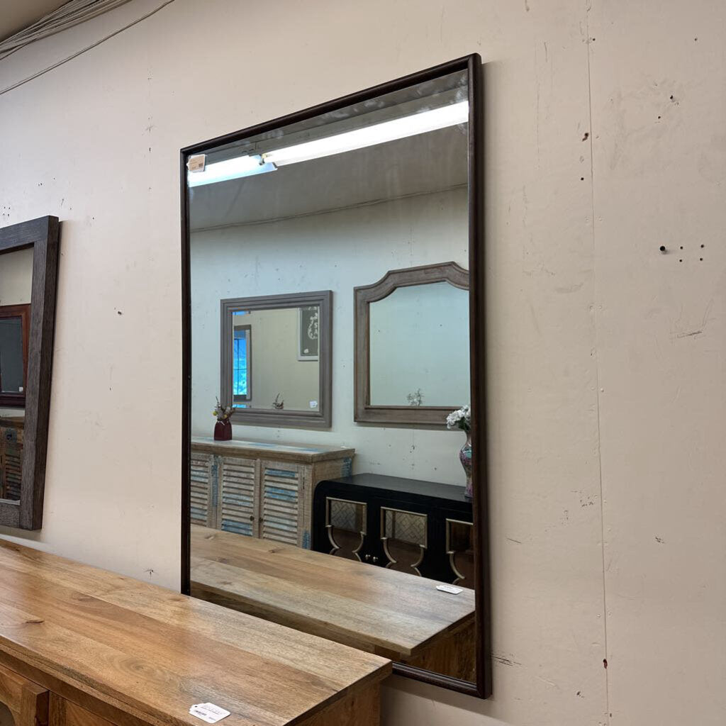 Large mirror with wooden frame on a wall, reflecting other mirrors and furniture.