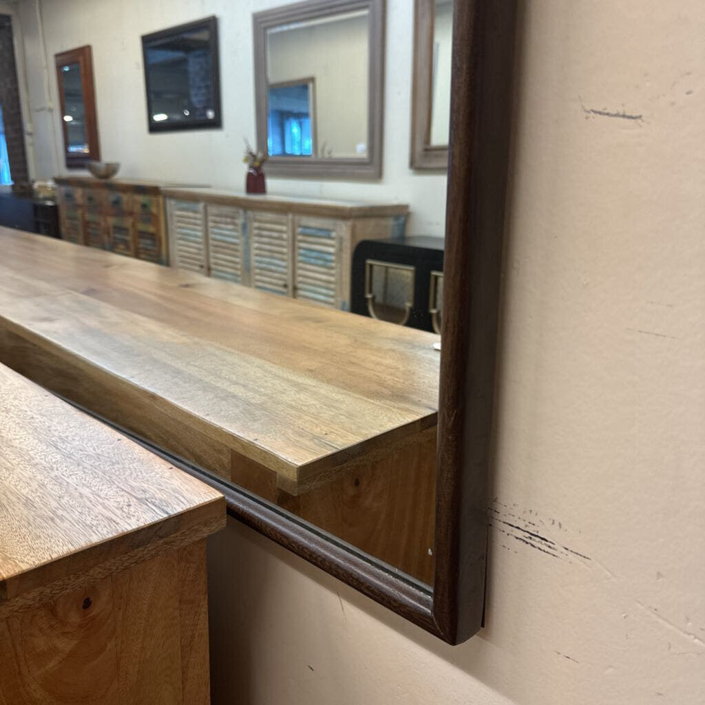 Wooden counter with a large mirror reflecting an interior setting.