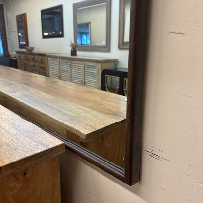 Wooden counter with a large mirror reflecting an interior setting.