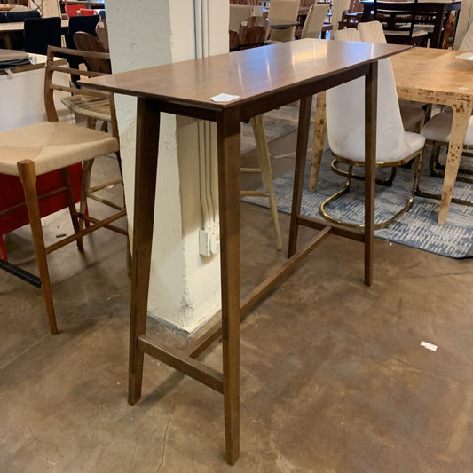 Wooden bar height table in a showroom setting with chairs and tables in the background.