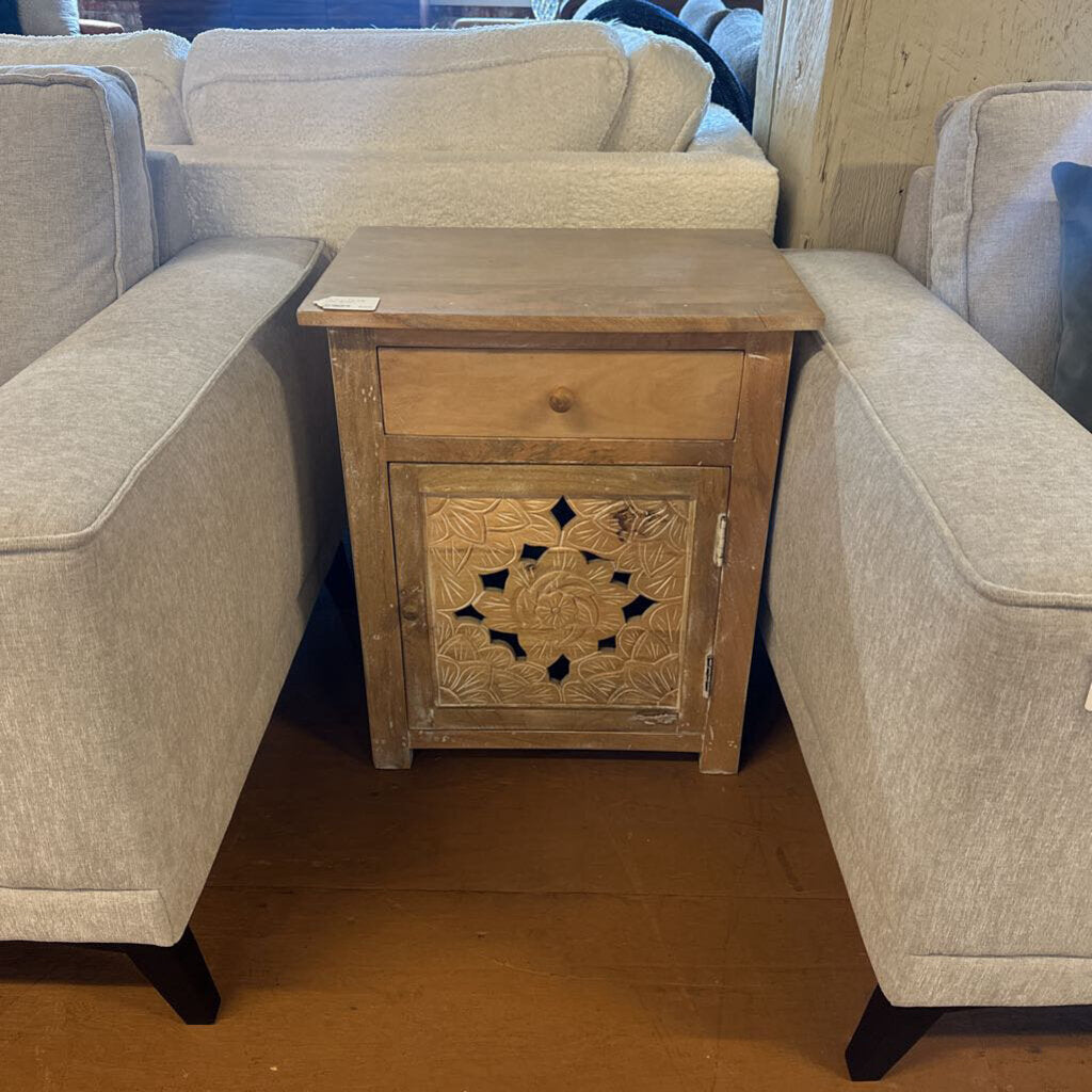 Wooden side table with carvings between two beige armchairs.