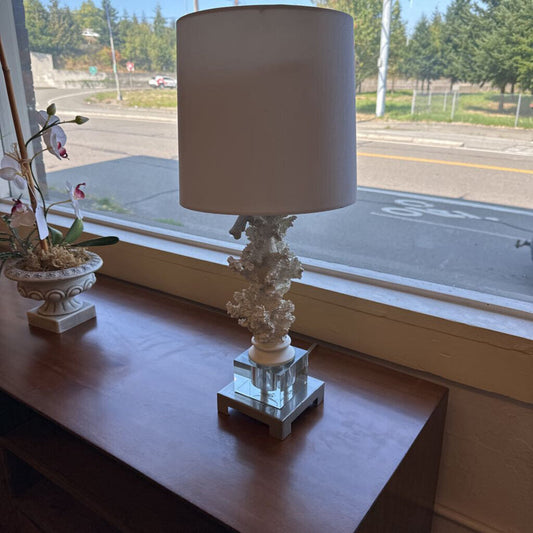 Decorative lamp with a white shade on a wooden surface near a window.