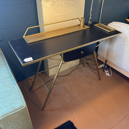 Black desk with gold legs against a blue wall