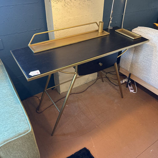 Black desk with gold legs against a blue wall