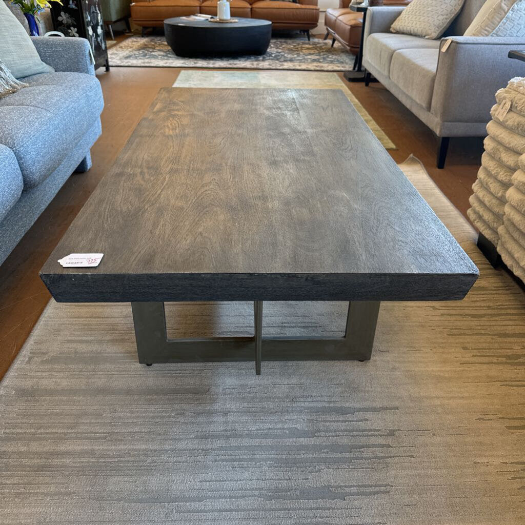 Large dark wooden coffee table in a living room setting with gray sofas and a rug.
