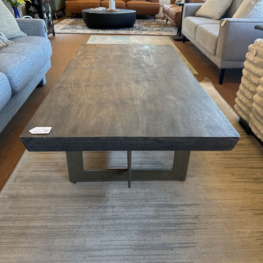 Large dark wooden coffee table in a living room setting with gray sofas and a rug.