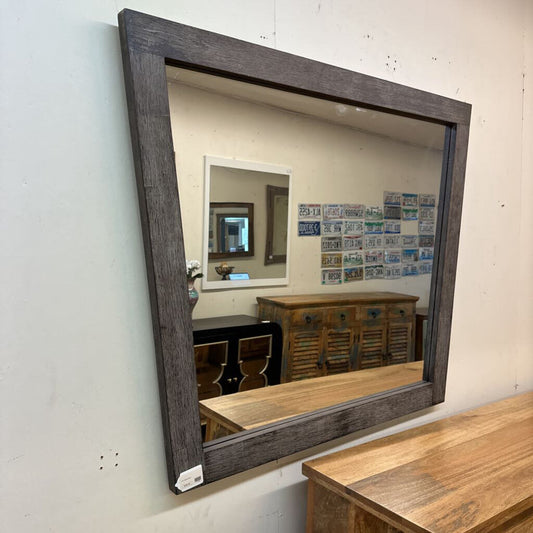 Wooden-framed mirror on a wall with a dining room reflection.