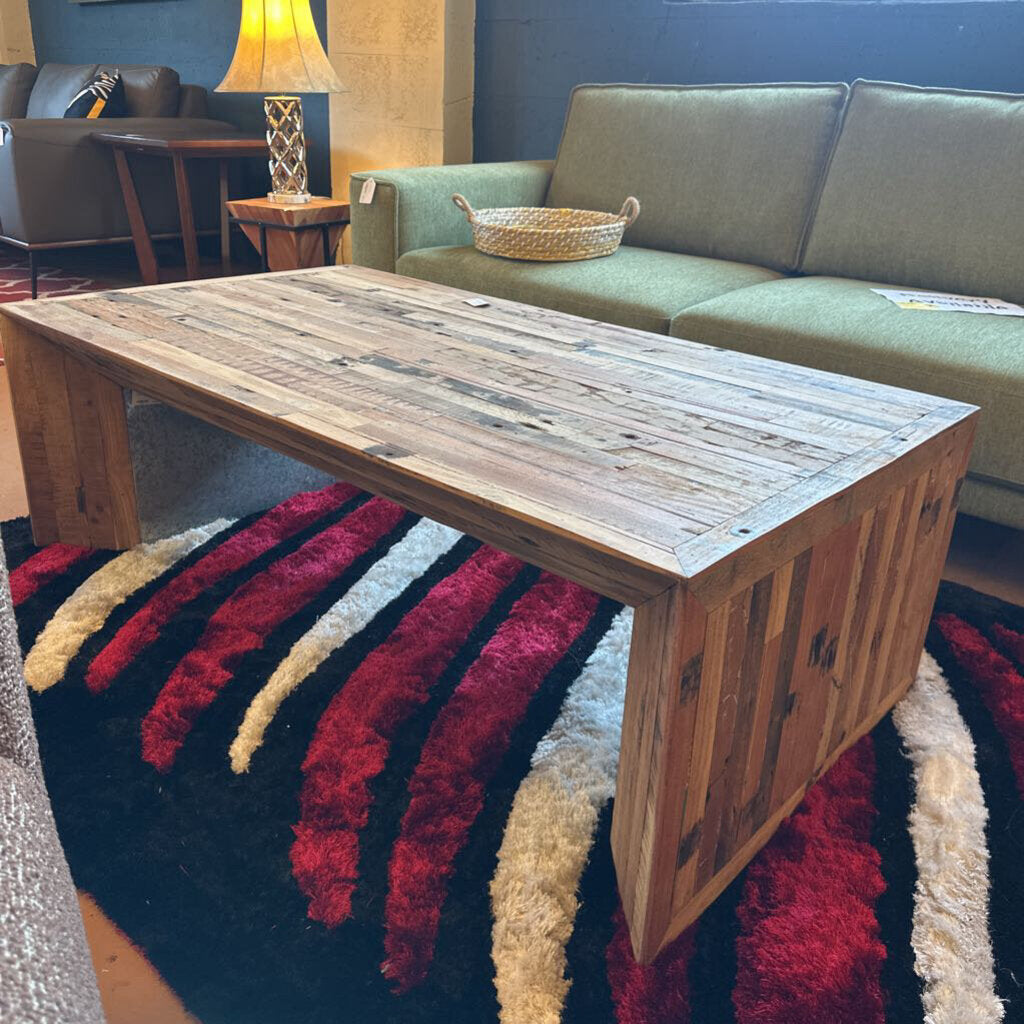 Wooden coffee table in a living room with a green sofa and colorful rug.