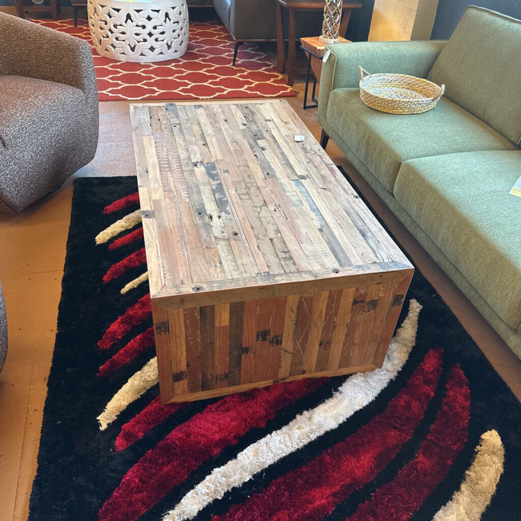 Wooden coffee table in a living room setting with a green sofa and patterned rug.
