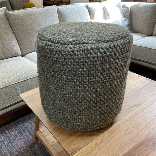 Textured green ottoman on a wooden table with a gray sofa in the background