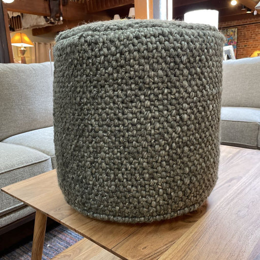 Textured green ottoman on a wooden table in a living room setting.