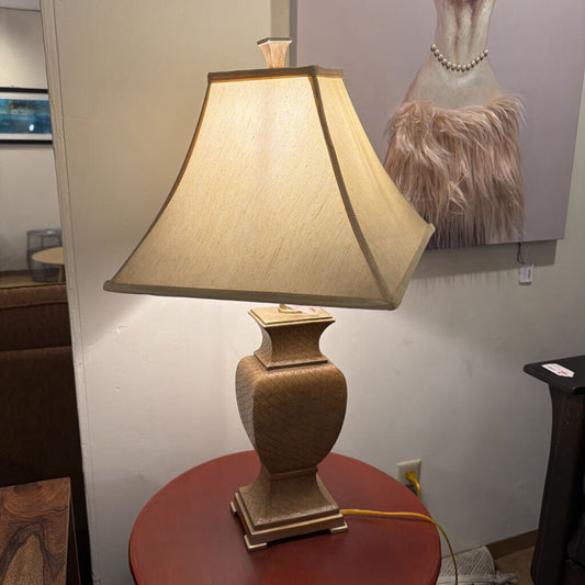 Decorative table lamp on a round red table with a neutral wall and artwork in the background.