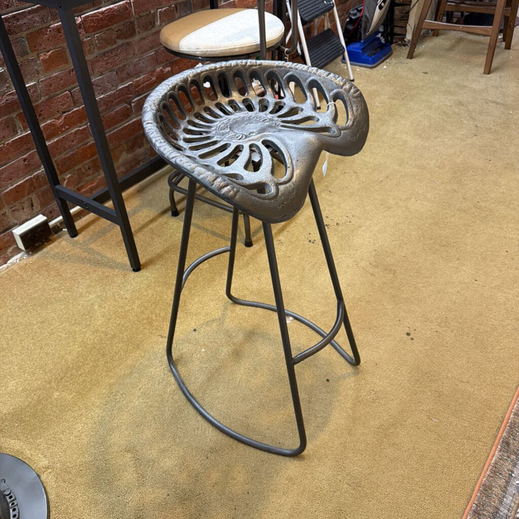 Cast iron bar stool with decorative backrest on a beige floor.