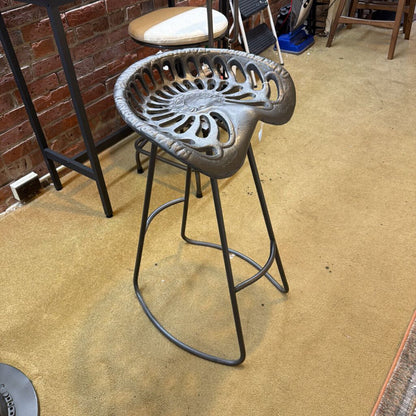 Cast iron bar stool with decorative backrest on a beige floor.