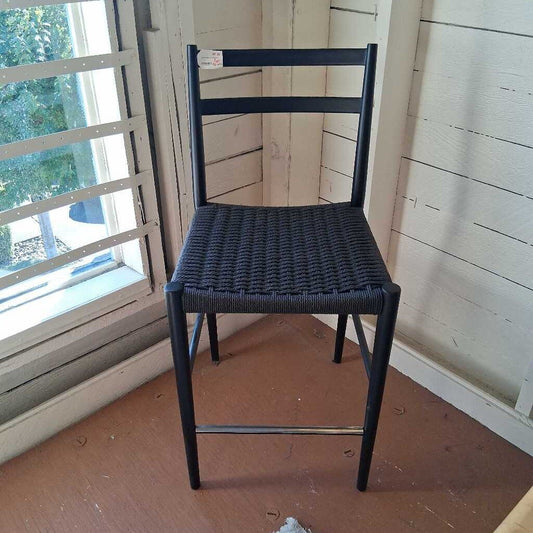 Black metal chair with woven seat in a room with wooden floor and window.