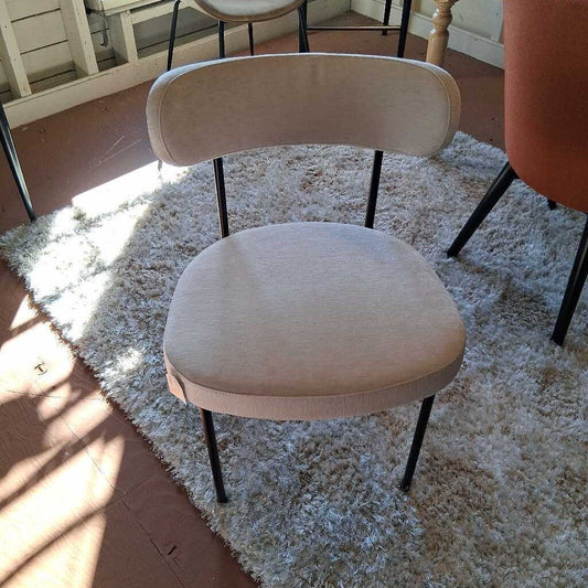 Beige chair on a textured rug with sunlight casting shadows