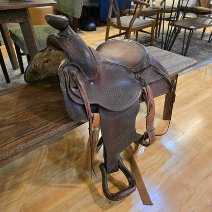Brown leather saddle on a wooden bench in an indoor setting