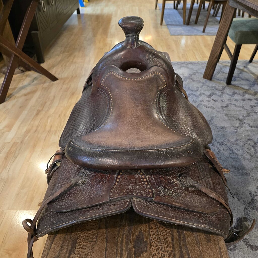 Brown leather saddle on a wooden floor with furniture in the background