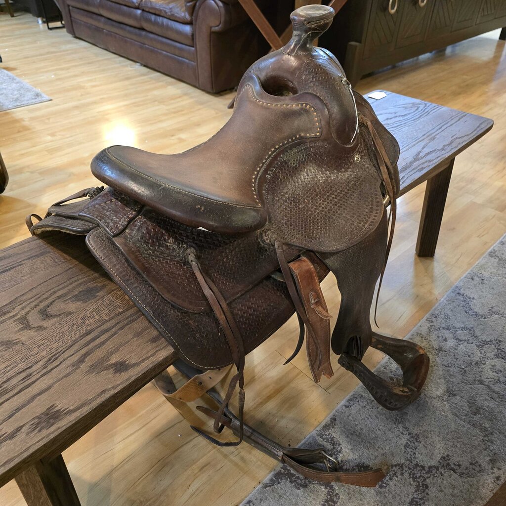Brown leather saddle on a wooden table in a room with wooden flooring and furniture.