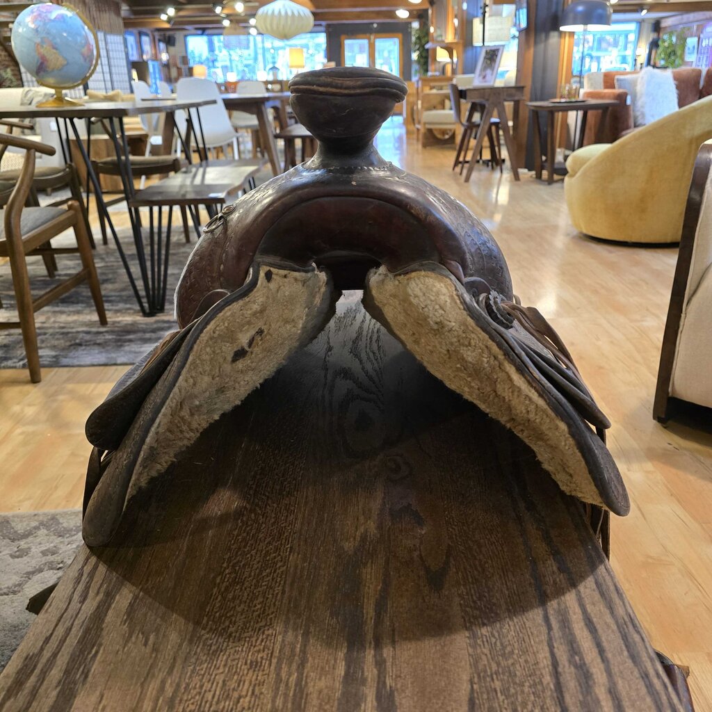 Brown leather saddle on a wooden table with a blurred indoor setting