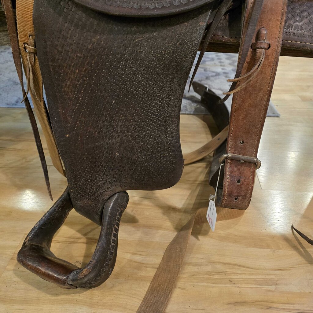Brown leather saddle on a wooden floor with a tag attached