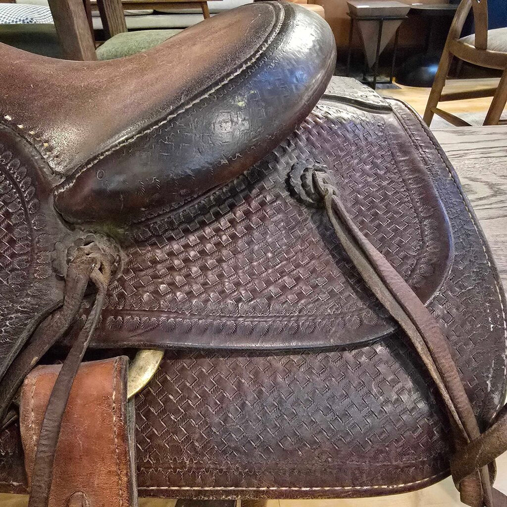 Brown leather saddle with intricate patterns on a wooden floor.