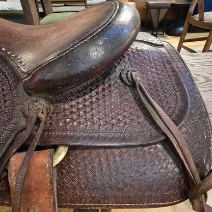 Brown leather saddle with intricate patterns on a wooden floor.
