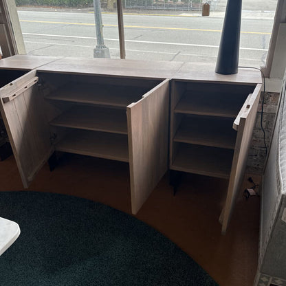 Wooden L-shaped desk with open shelves in a room with a window.