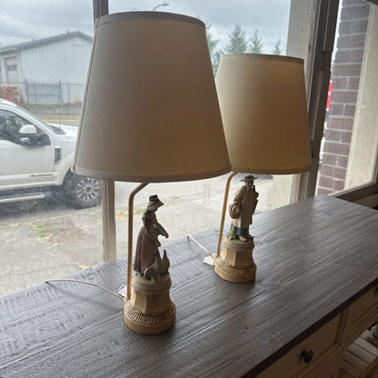 Two table lamps with beige shades and decorative bases on a wooden surface.