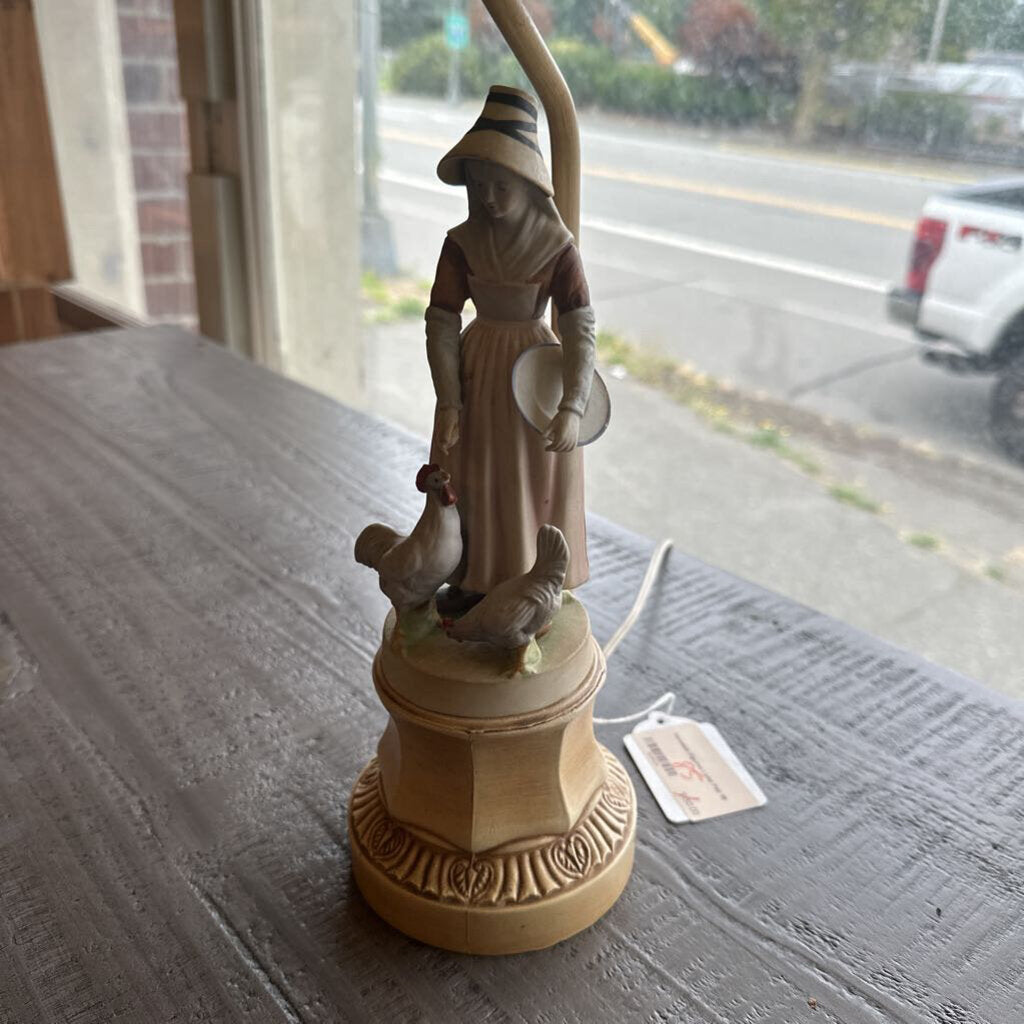 Statue of a woman with chickens on a pedestal, placed on a table.